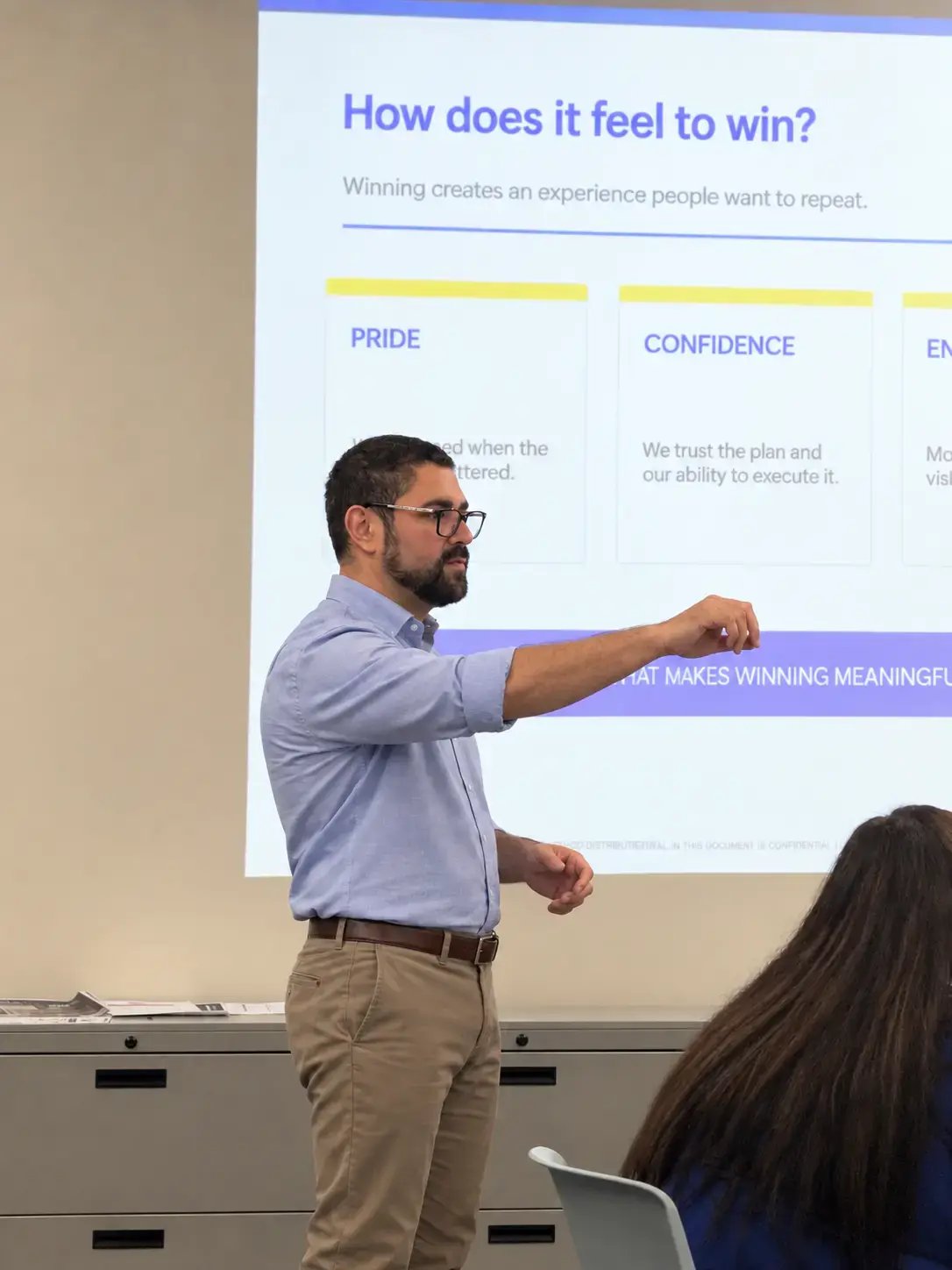 Presenter leading a business workshop in front of a projected slide while speaking to seated attendees.